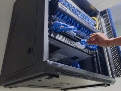 A network technician is setting up and configuring the patch panel and router switch in the wall-mounted cabinet.